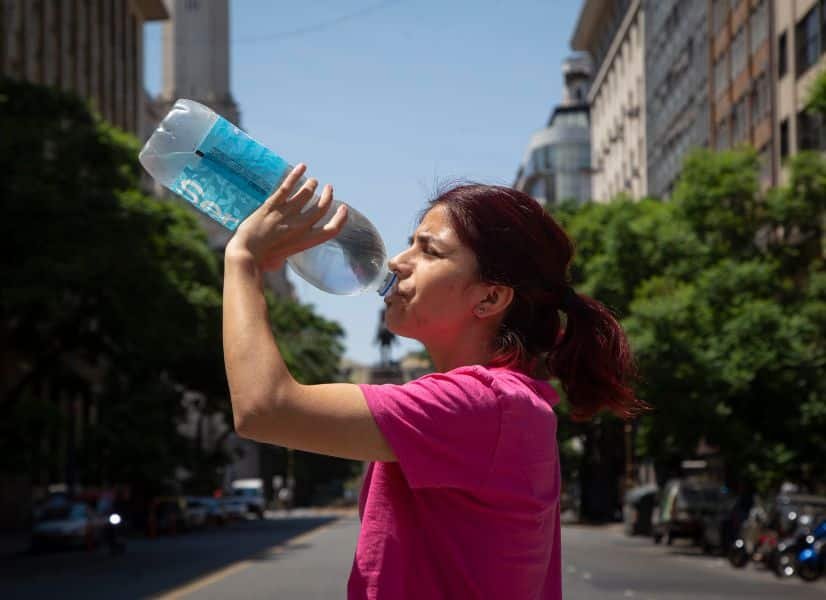 Una mujer acalorada toma agua de una botella en la ciudad.