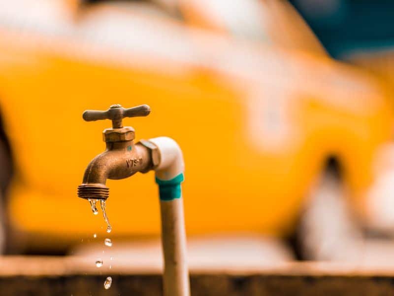 Una canilla o grifo con un fondo naranja. De la canilla salen unas pocas gotas de agua