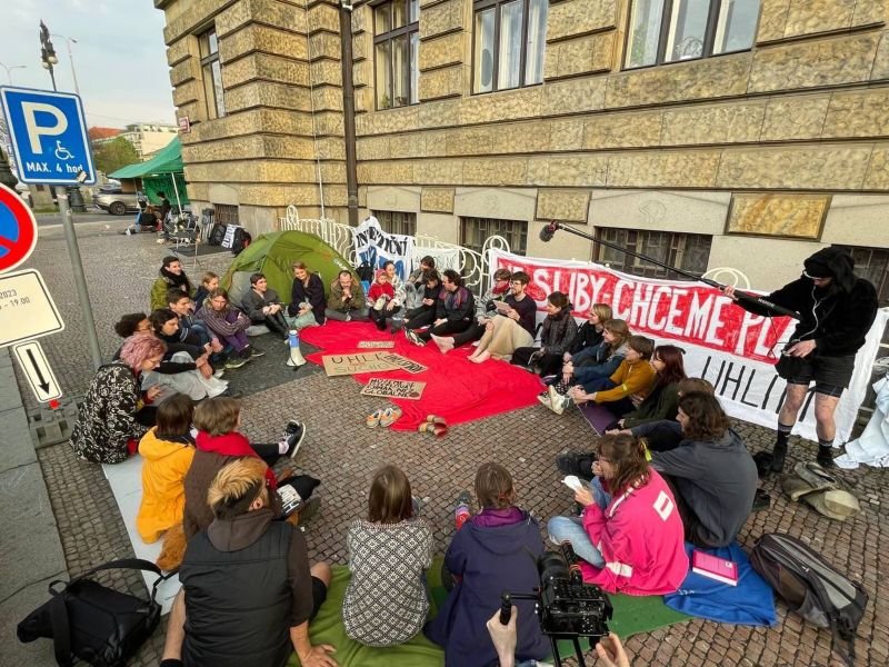 Un grupo de alumnos universitarios en el exterior de su universidad. Están todos sentados en ronda. Tienen carteles de la campaña End Fossil: Occupy!