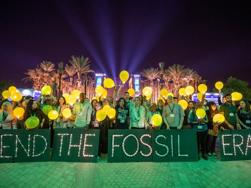 personas en la COP28 con carteles que dicen "Terminar con la era de los combustibles fósiles".