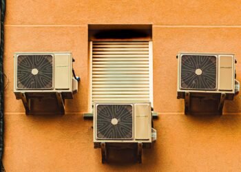 Unidades de aire acondicionado instaladas en la fachada de un edificio urbano expulsando aire caliente.