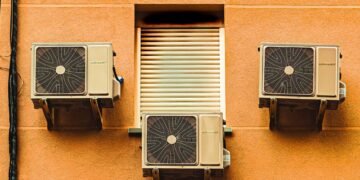 Unidades de aire acondicionado instaladas en la fachada de un edificio urbano expulsando aire caliente.