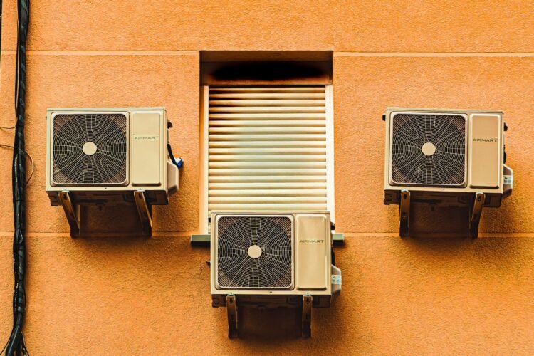 Unidades de aire acondicionado instaladas en la fachada de un edificio urbano expulsando aire caliente.