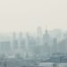 Niebla tóxica sobre una ciudad con edificios, representando la contaminación del aire que afecta la salud infantil.