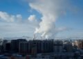 Vista de una ciudad con contaminación atmosférica visible y emisiones industriales en el horizonte.