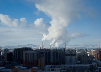 Vista de una ciudad con contaminación atmosférica visible y emisiones industriales en el horizonte.