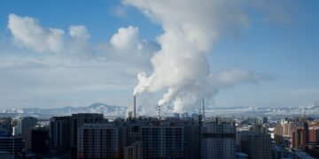Vista de una ciudad con contaminación atmosférica visible y emisiones industriales en el horizonte.