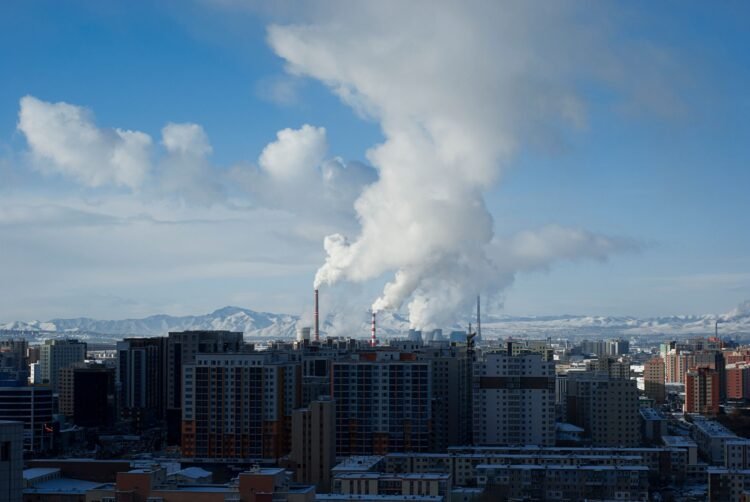 Vista de una ciudad con contaminación atmosférica visible y emisiones industriales en el horizonte.