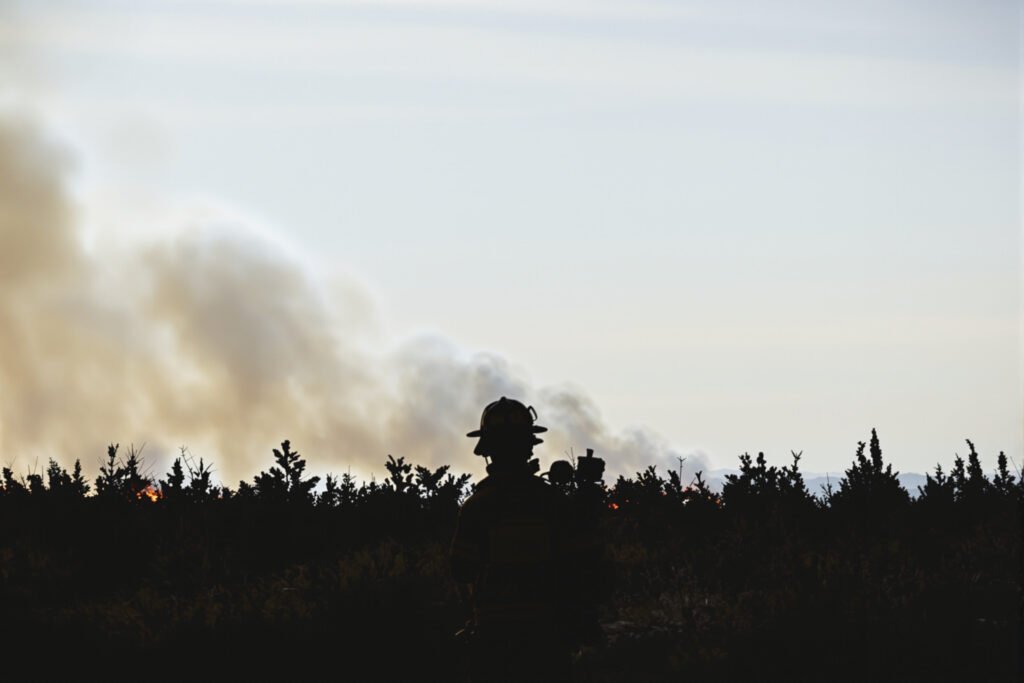 Silueta de bombero forestal frente a incendio forestal en Estados Unidos, con humo denso al fondo.