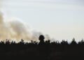 Silueta de bombero forestal frente a incendio forestal en Estados Unidos, con humo denso al fondo.