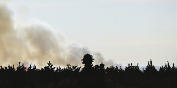 Silueta de bombero forestal frente a incendio forestal en Estados Unidos, con humo denso al fondo.