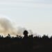 Silueta de bombero forestal frente a incendio forestal en Estados Unidos, con humo denso al fondo.