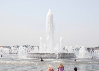 Una fuente pública en una plaza europea durante una ola de calor extremo, con personas buscando alivio del calor sofocante.