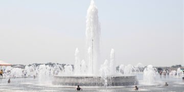 Una fuente pública en una plaza europea durante una ola de calor extremo, con personas buscando alivio del calor sofocante.