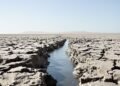 Lecho seco y agrietado de un río europeo durante sequía extrema, con barcos varados en el horizonte.