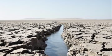 Lecho seco y agrietado de un río europeo durante sequía extrema, con barcos varados en el horizonte.
