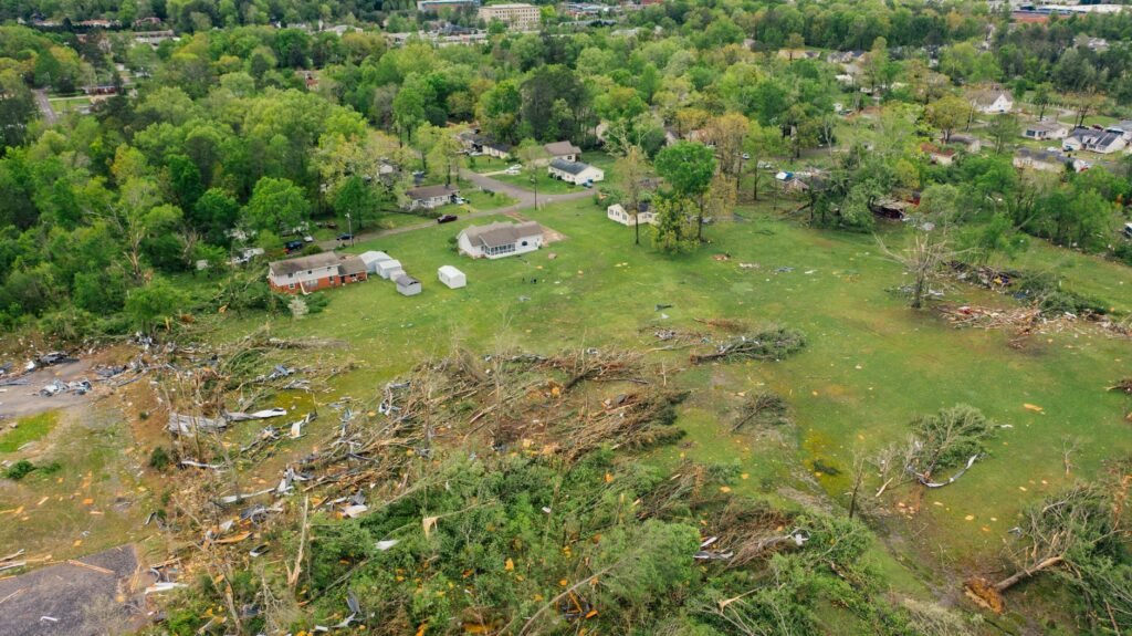 Paisaje rural con restos de un tornado, árboles caídos y viviendas dañadas tras un fenómeno meteorológico extremo.