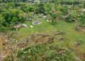 Paisaje rural con restos de un tornado, árboles caídos y viviendas dañadas tras un fenómeno meteorológico extremo.