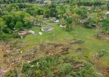Paisaje rural con restos de un tornado, árboles caídos y viviendas dañadas tras un fenómeno meteorológico extremo.