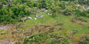 Paisaje rural con restos de un tornado, árboles caídos y viviendas dañadas tras un fenómeno meteorológico extremo.