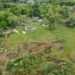 Paisaje rural con restos de un tornado, árboles caídos y viviendas dañadas tras un fenómeno meteorológico extremo.