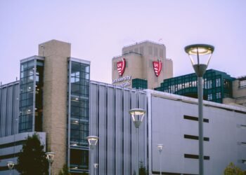 Fachada acristalada de un hospital moderno con luz solar reflejándose en las ventanas.