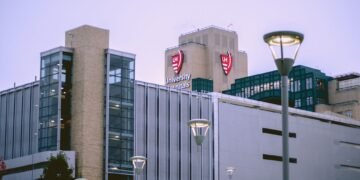 Fachada acristalada de un hospital moderno con luz solar reflejándose en las ventanas.
