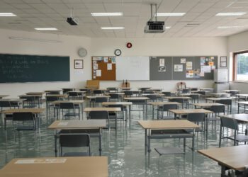 Aula de escuela inundada con bancos vacíos, símbolo del impacto del clima en la educación global.