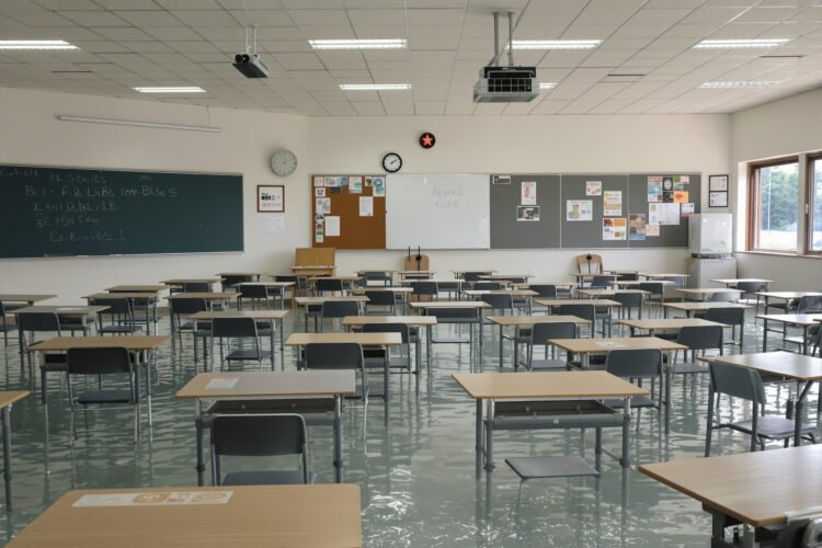 Aula de escuela inundada con bancos vacíos, símbolo del impacto del clima en la educación global.