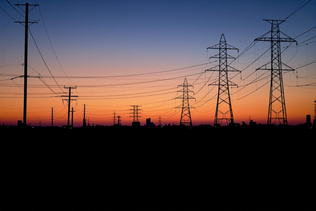 Líneas de transmisión eléctrica al atardecer sobre una ciudad, representando la infraestructura energética del AMBA.