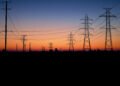 Líneas de transmisión eléctrica al atardecer sobre una ciudad, representando la infraestructura energética del AMBA.