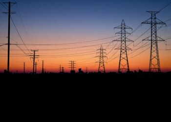 Líneas de transmisión eléctrica al atardecer sobre una ciudad, representando la infraestructura energética del AMBA.