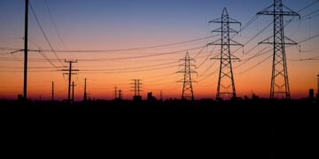 Líneas de transmisión eléctrica al atardecer sobre una ciudad, representando la infraestructura energética del AMBA.