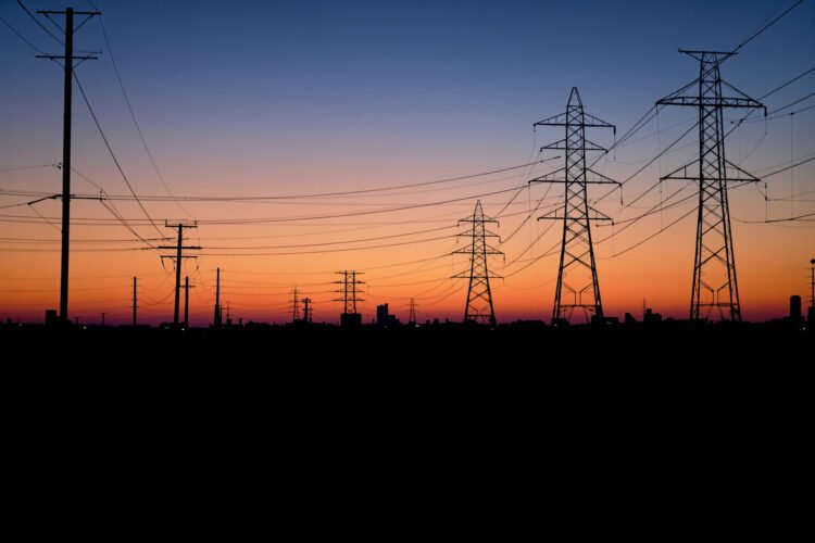 Líneas de transmisión eléctrica al atardecer sobre una ciudad, representando la infraestructura energética del AMBA.