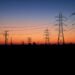 Líneas de transmisión eléctrica al atardecer sobre una ciudad, representando la infraestructura energética del AMBA.