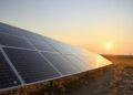 Paneles solares instalados en un campo abierto cerca de infraestructura aeroportuaria al atardecer.
