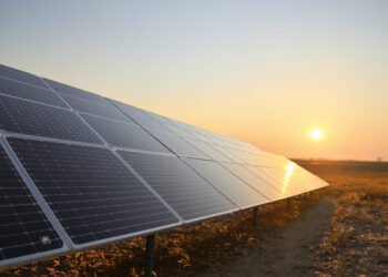 Paneles solares instalados en un campo abierto cerca de infraestructura aeroportuaria al atardecer.