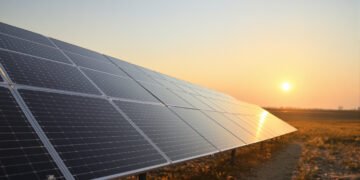 Paneles solares instalados en un campo abierto cerca de infraestructura aeroportuaria al atardecer.