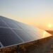 Paneles solares instalados en un campo abierto cerca de infraestructura aeroportuaria al atardecer.