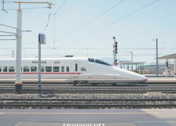 Andén de estación de tren de alta velocidad con vías y cielo despejado.