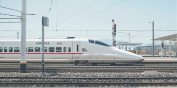 Andén de estación de tren de alta velocidad con vías y cielo despejado.