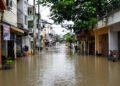 Calles inundadas en una ciudad asiática durante la temporada de monzones, con edificios reflejados en el agua.