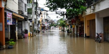 Calles inundadas en una ciudad asiática durante la temporada de monzones, con edificios reflejados en el agua.