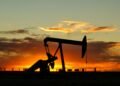Refinería de petróleo con chimeneas emitiendo gases al atardecer, simbolizando la dependencia de combustibles fósiles.