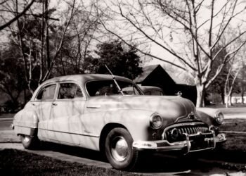Autopista suburbana estadounidense con autos vintage, símbolo del Sueño Americano inventado por la industria petrolera.
