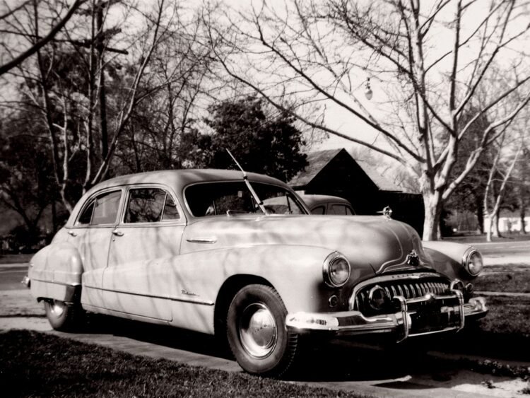 Autopista suburbana estadounidense con autos vintage, símbolo del Sueño Americano inventado por la industria petrolera.