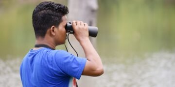 Observador de aves en la naturaleza documentando biodiversidad con binoculares