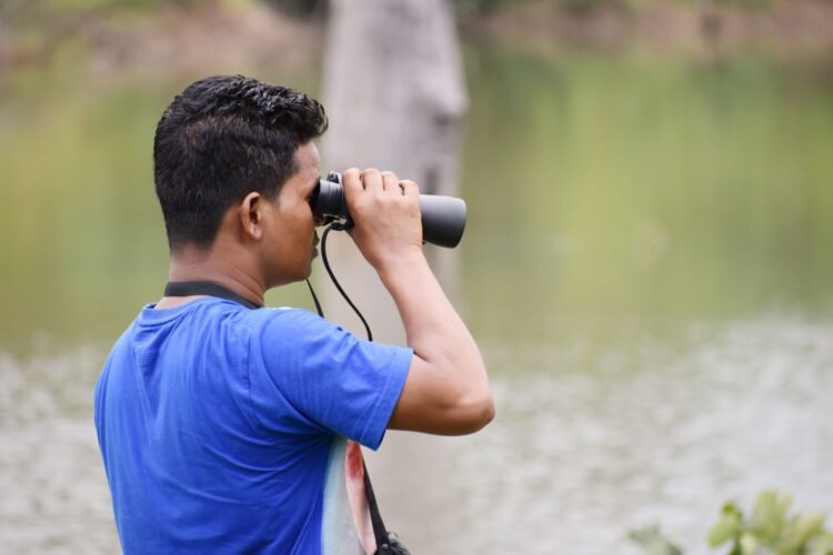 Observador de aves en la naturaleza documentando biodiversidad con binoculares