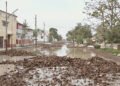 Calle inundada con agua fangosa y escombros tras lluvias torrenciales en zona urbana.