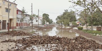 Calle inundada con agua fangosa y escombros tras lluvias torrenciales en zona urbana.